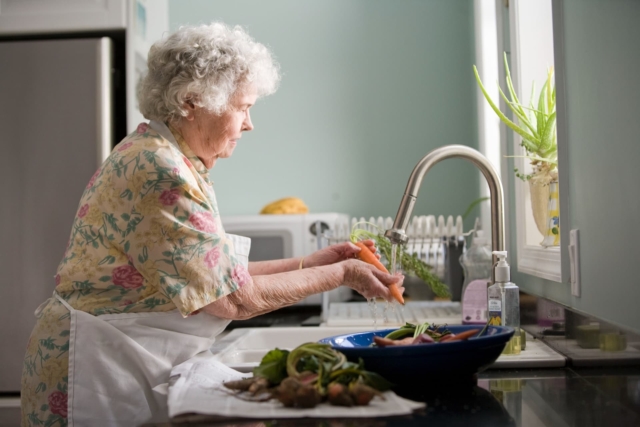 An older lady washing vegetables.