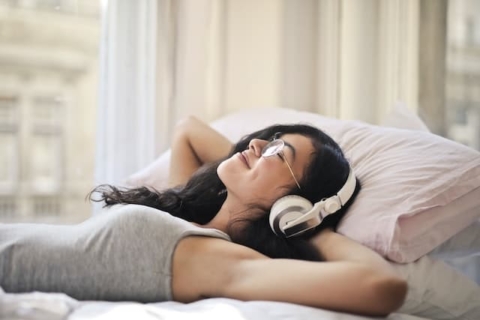 Woman relaxing on the bad, listening to music.