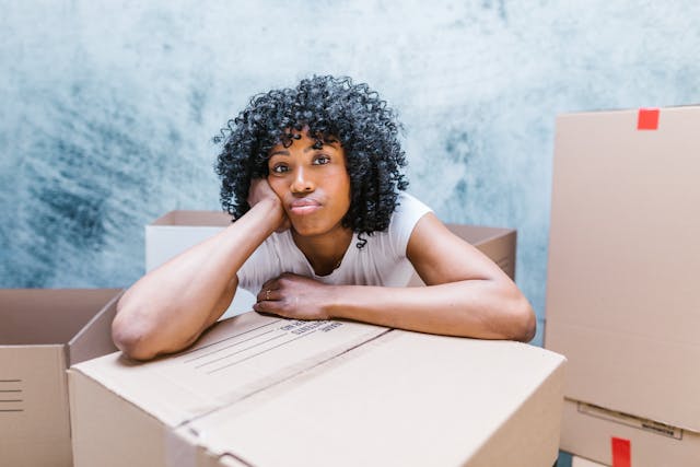 Young woman looking sad and sitting next to a large moving box
